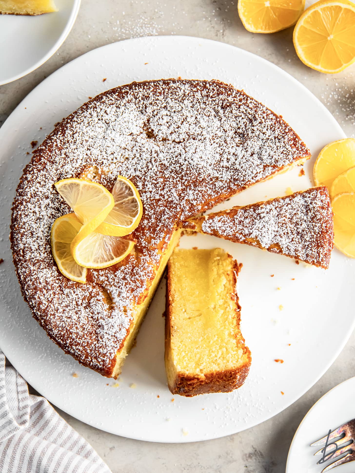 lemon olive oil cake with a few slices cut out and one on its side.