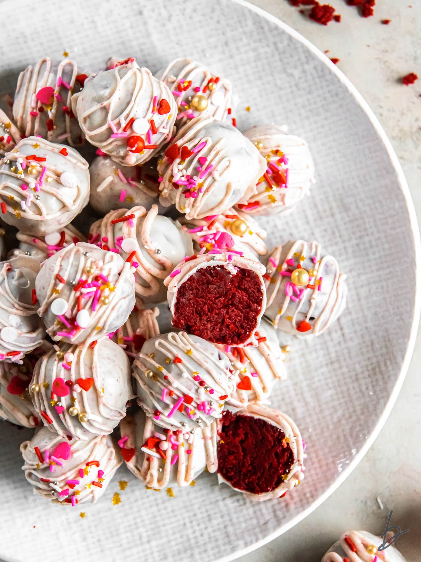 red velvet cake truffles with white chocolate and sprinkles on a plate with one ball cut in haf.