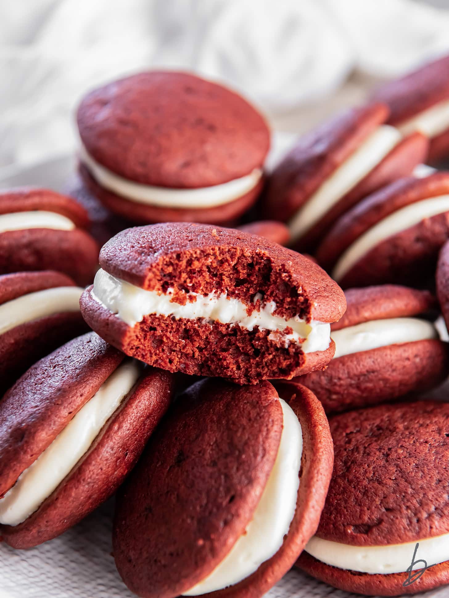red velvet whoopie pie with a bite taken out of it sitting on top of more whoopie pies.