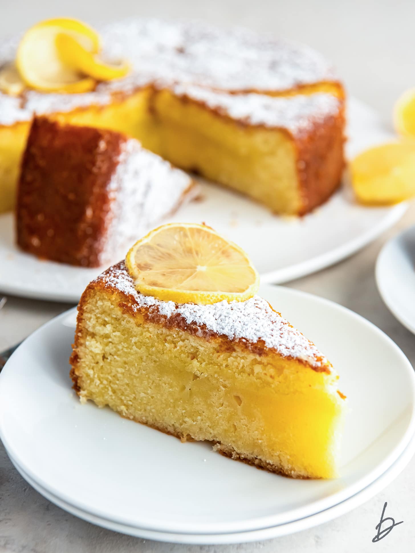 slice of lemon olive oil cake dusted with confectioners' sugar and garnished with a lemon slice.