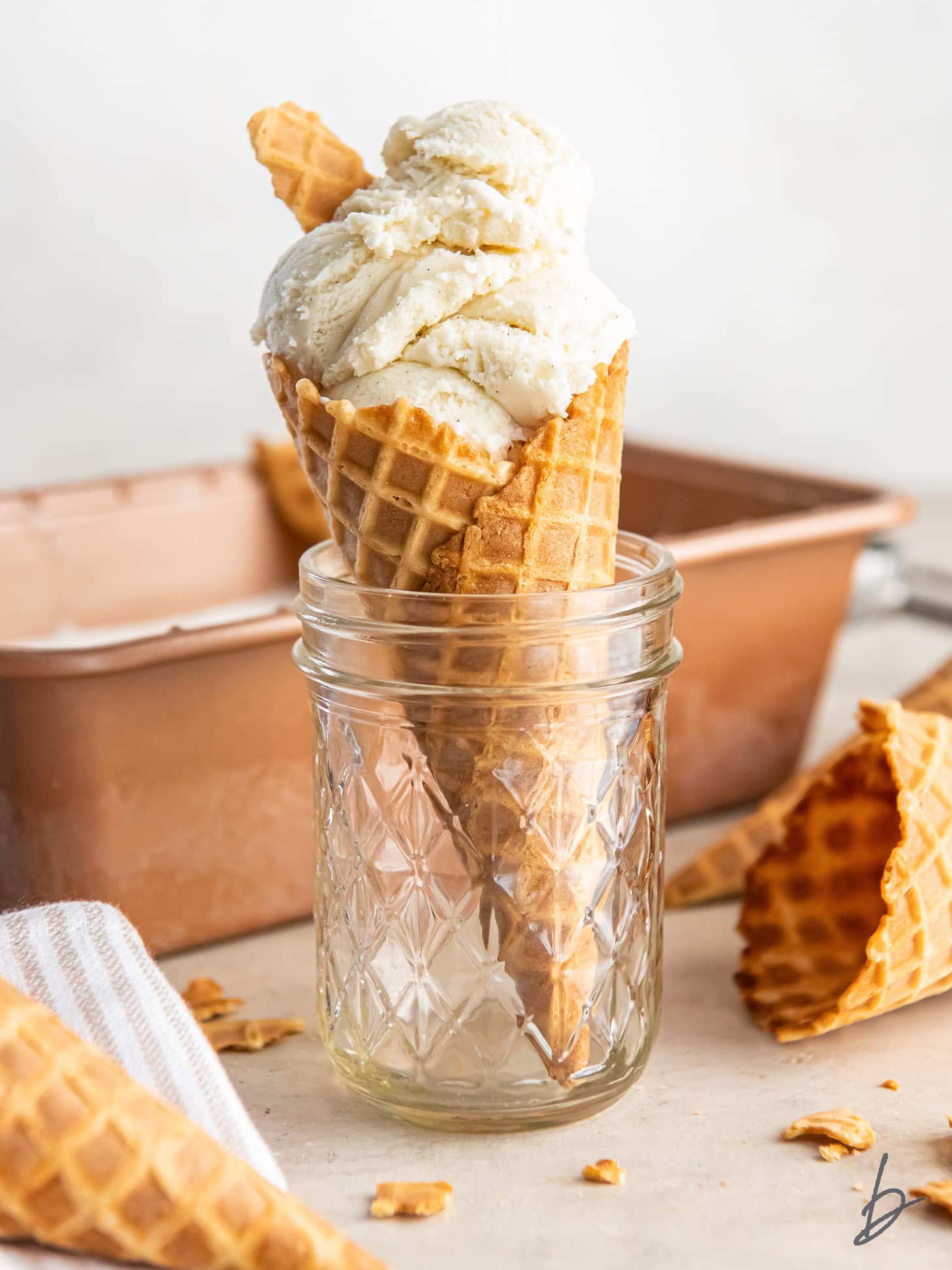 homemade vanilla ice cream in a waffle cone held up in a glass jar.