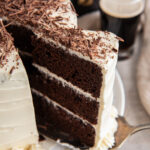 three layer chocolate guinness cake slice being pulled away from cake with baileys frosting and chocolate shavings.