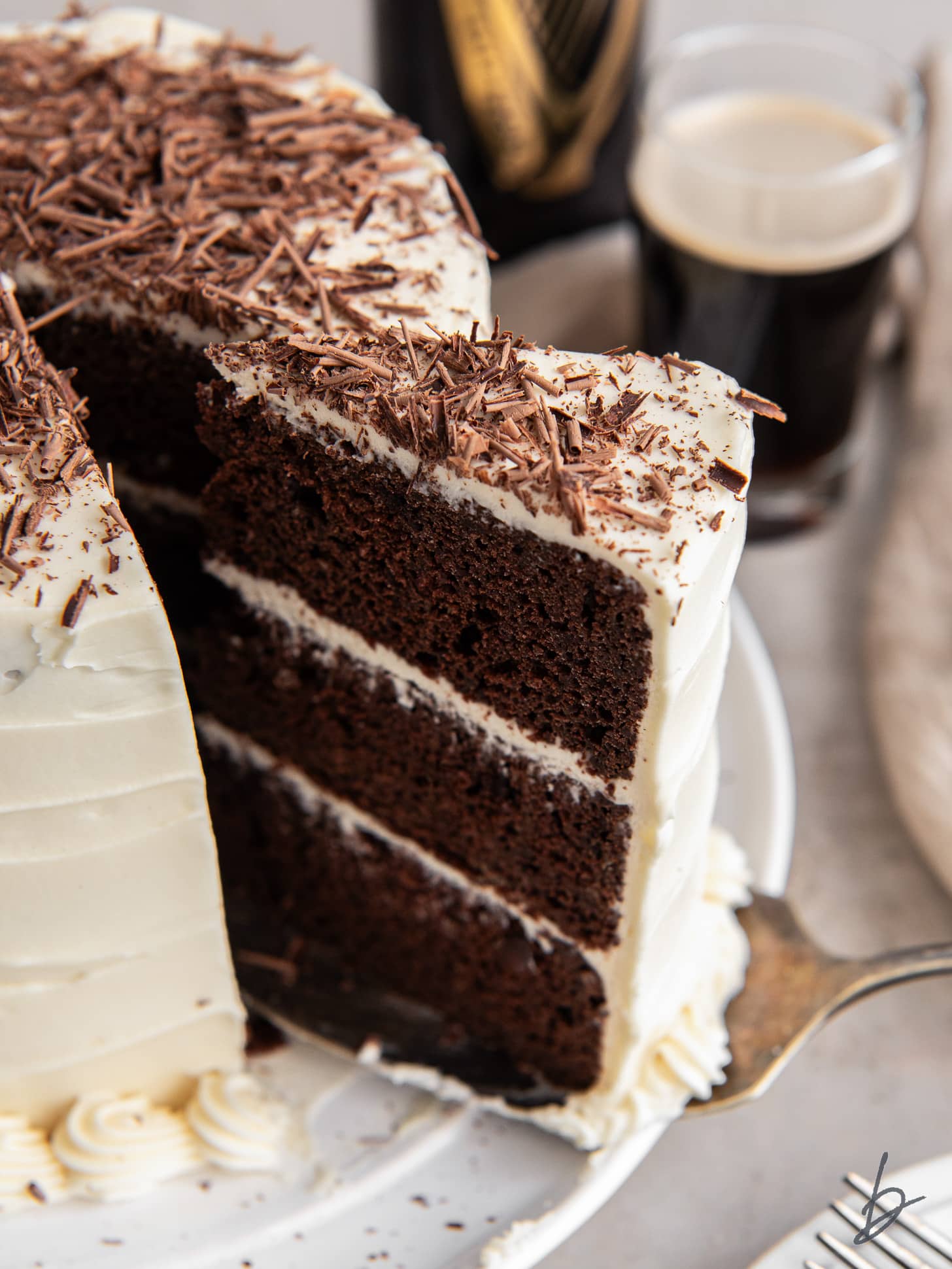three layer chocolate guinness cake slice being pulled away from cake with baileys frosting and chocolate shavings.