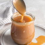 spoon drizzling caramel sauce into a glass jar.