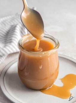 spoon drizzling caramel sauce into a glass jar.