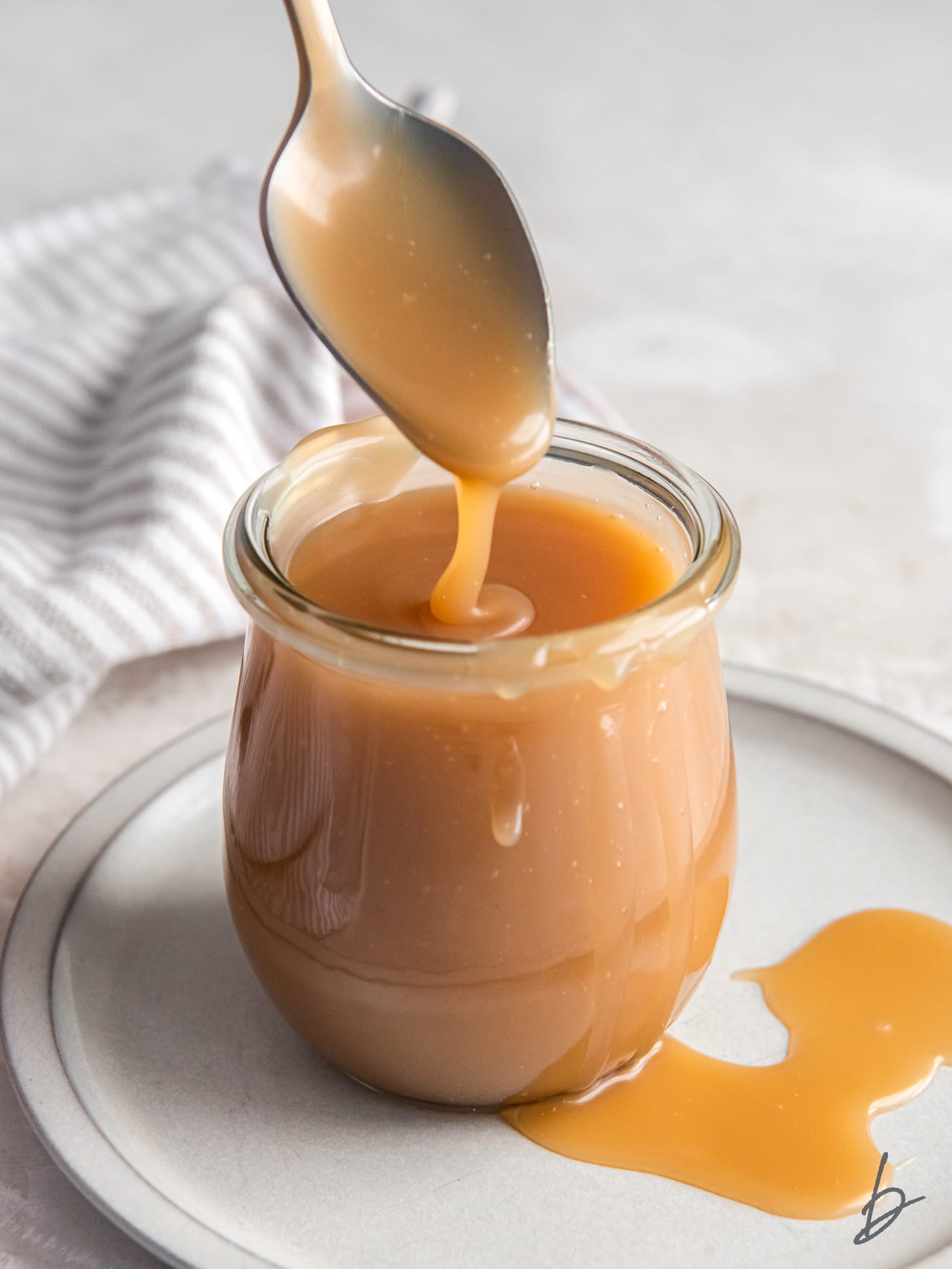 spoon drizzling caramel sauce into a glass jar.