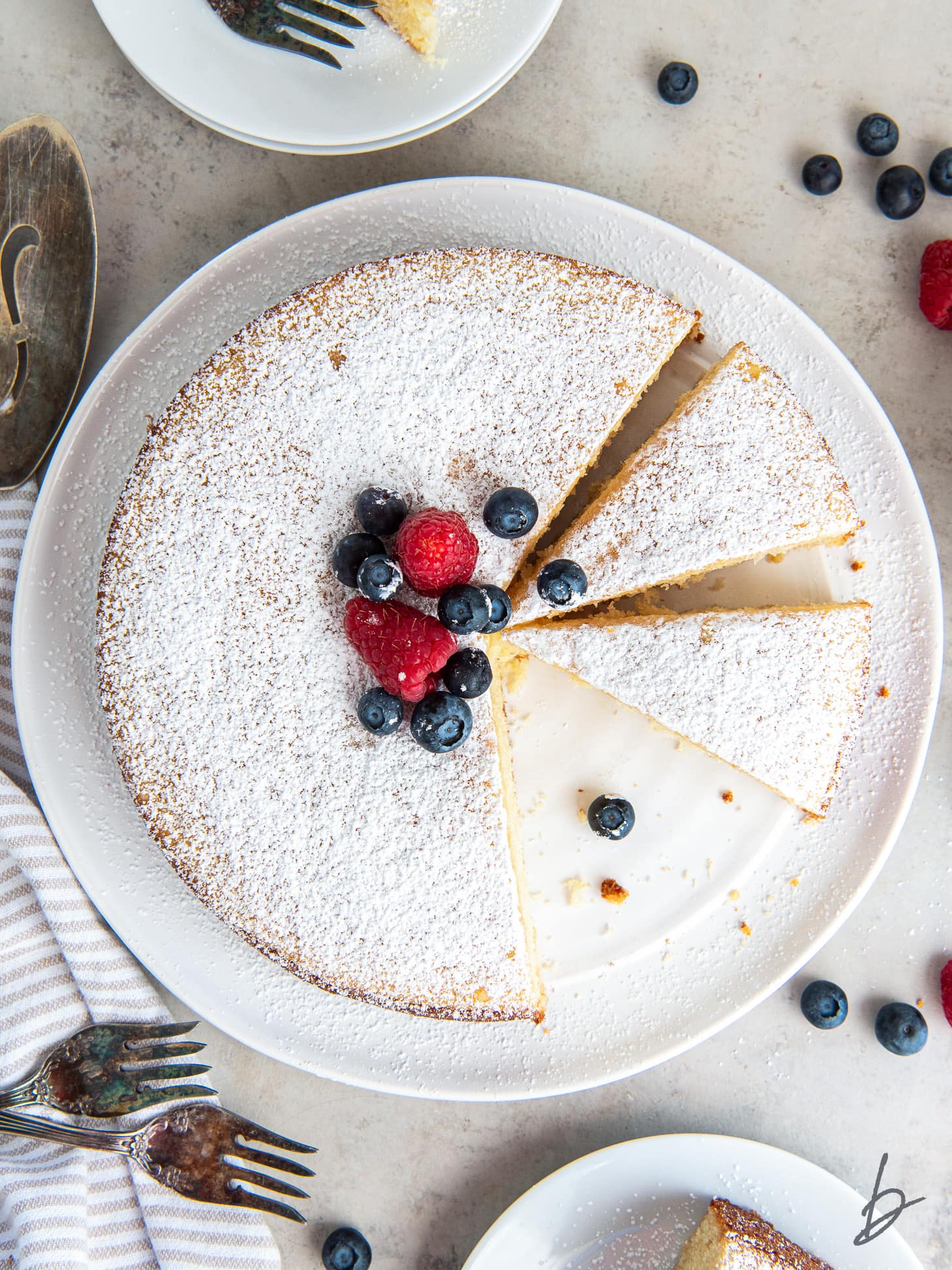 irish tea cake dusted with confectioners' sugar, topped with berries and one slice cut.