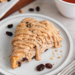 cinnamon raisins scone with cinnamon glaze on a white plate with a few raisins.