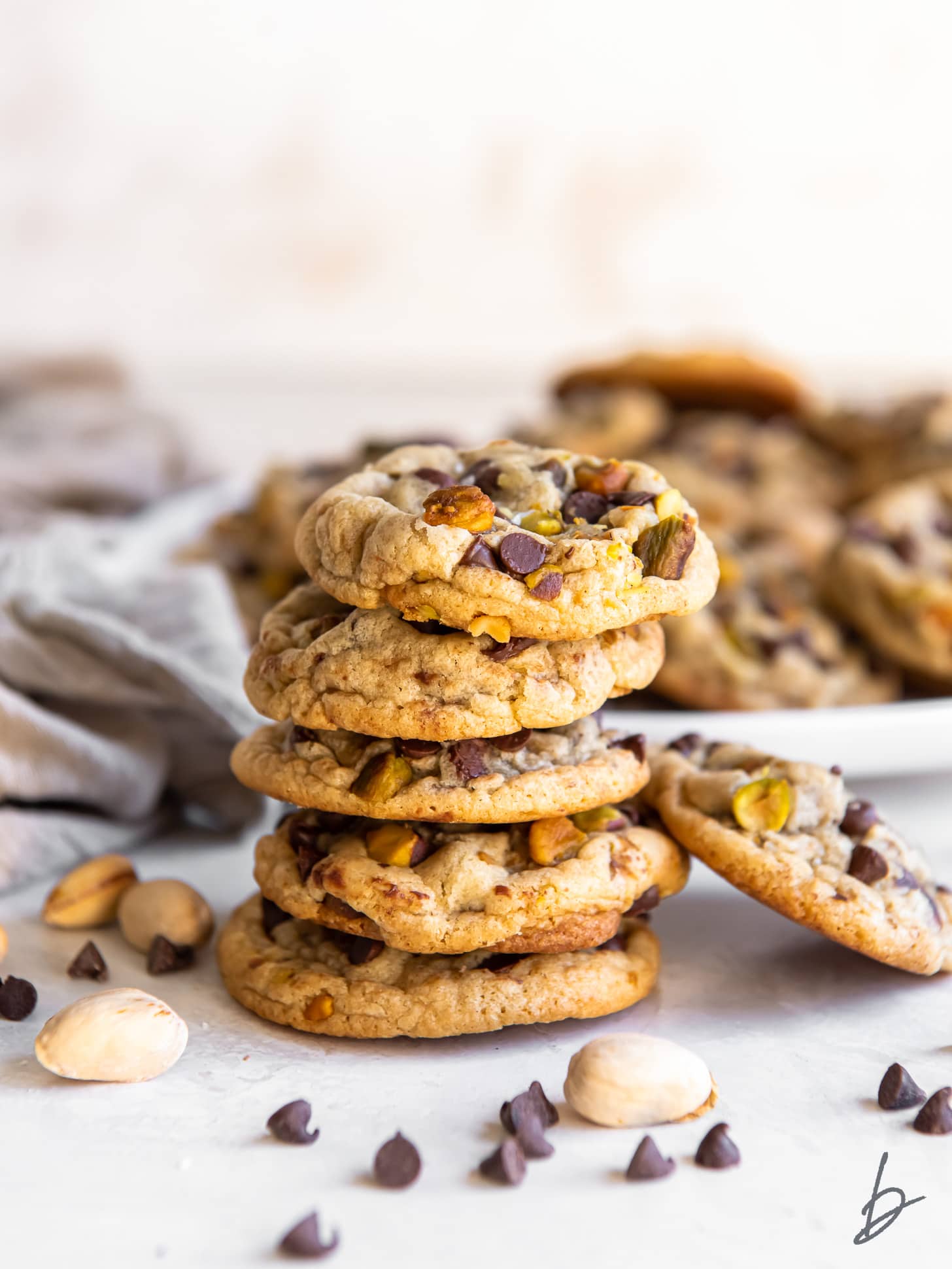 stack of salted chocolate chip pistachio cookies in front of a plate of more cookies.