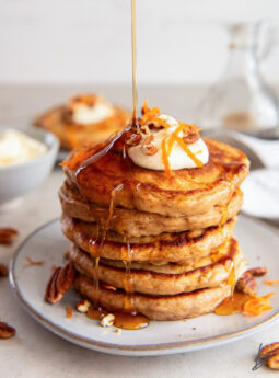 maple syrup poured on top and drizzling down a stack of carrot cake pancakes on a plate.