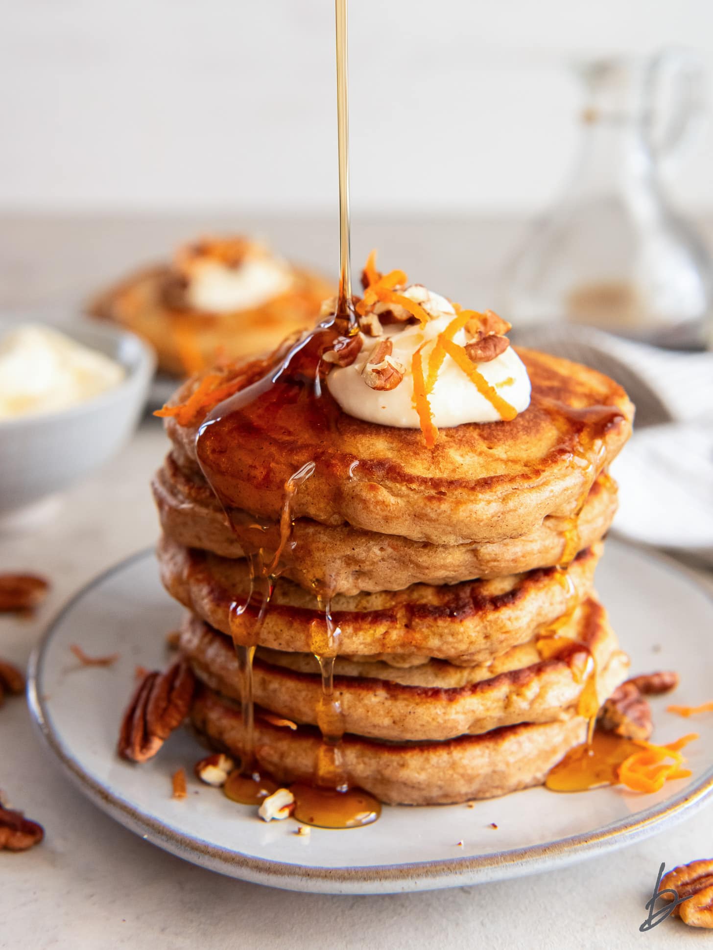 maple syrup poured on top and drizzling down a stack of carrot cake pancakes on a plate.