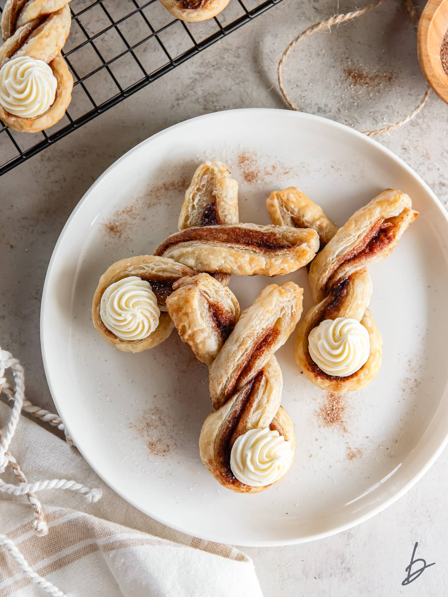 three easter bunny puff pastry twists with cream cheese frosting bunny tails on a white plate.