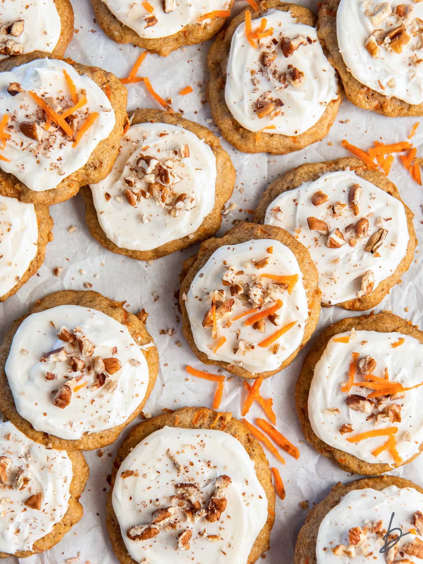 carrot cake cookies with cream cheese frosting garnished with chopped walnuts and carrot shreds.