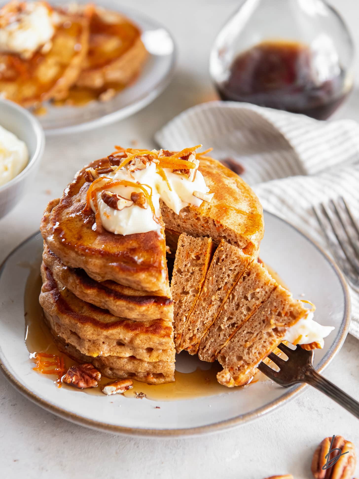 fork holding a bite of fluffy carrot cake pancakes taken from the stack on a plate.