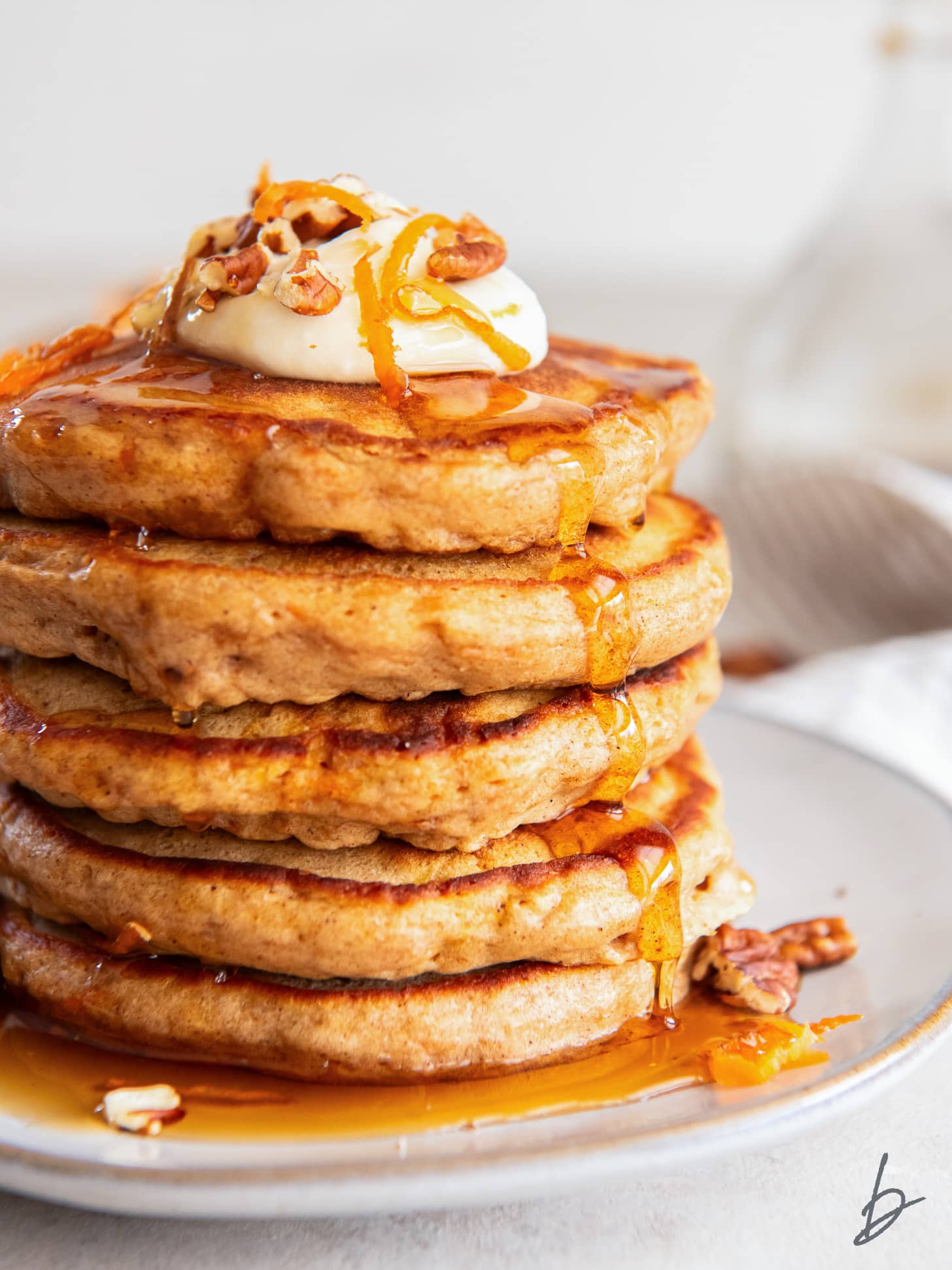 fluffy carrot cake pancakes topped with a dollop of whipped cream and maple syrup dripping down the sides.