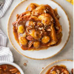 tabletop with plate of bananas foster french toast and chopped pecans garnish.