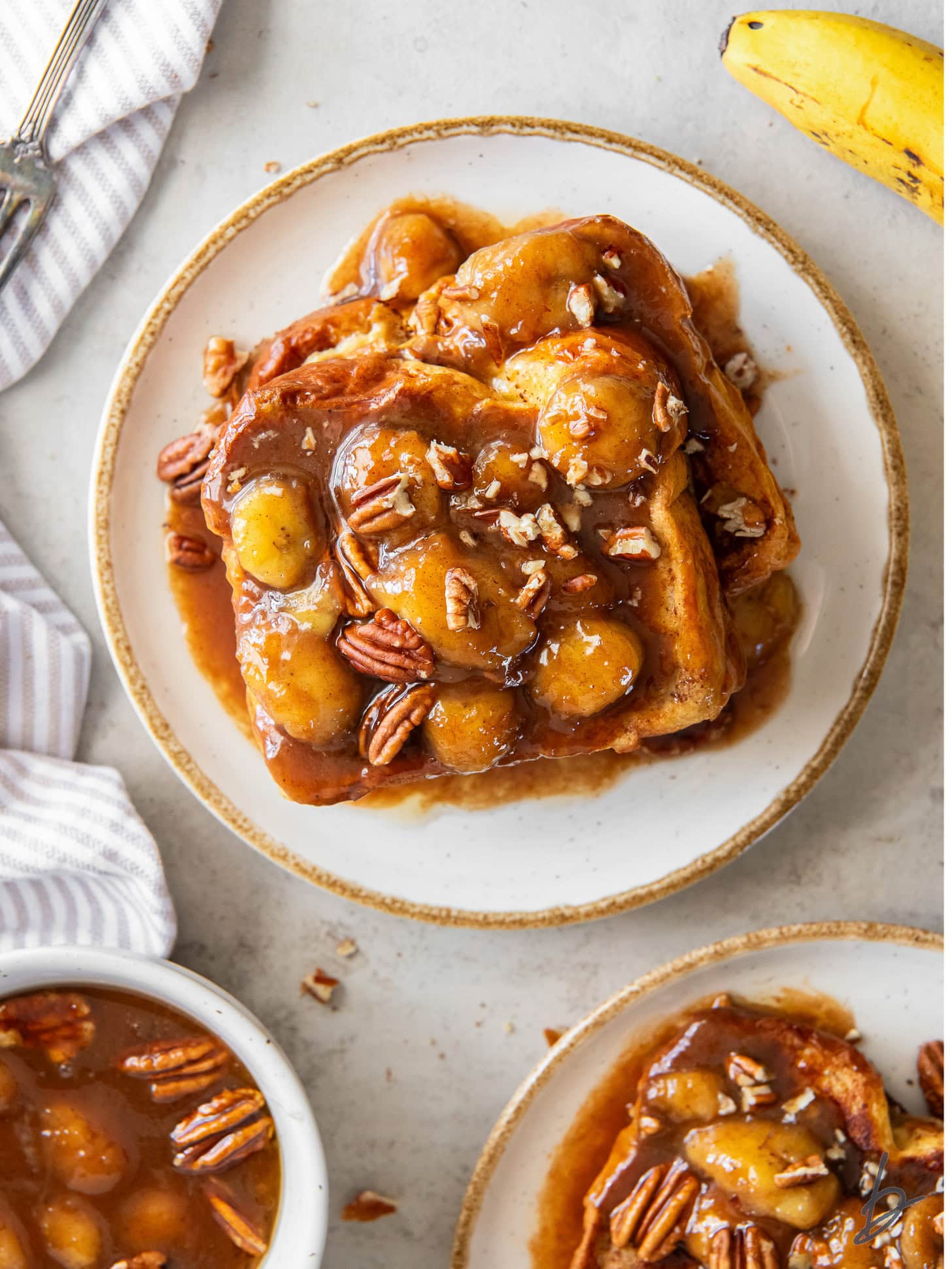 tabletop with plate of bananas foster french toast and chopped pecans garnish.