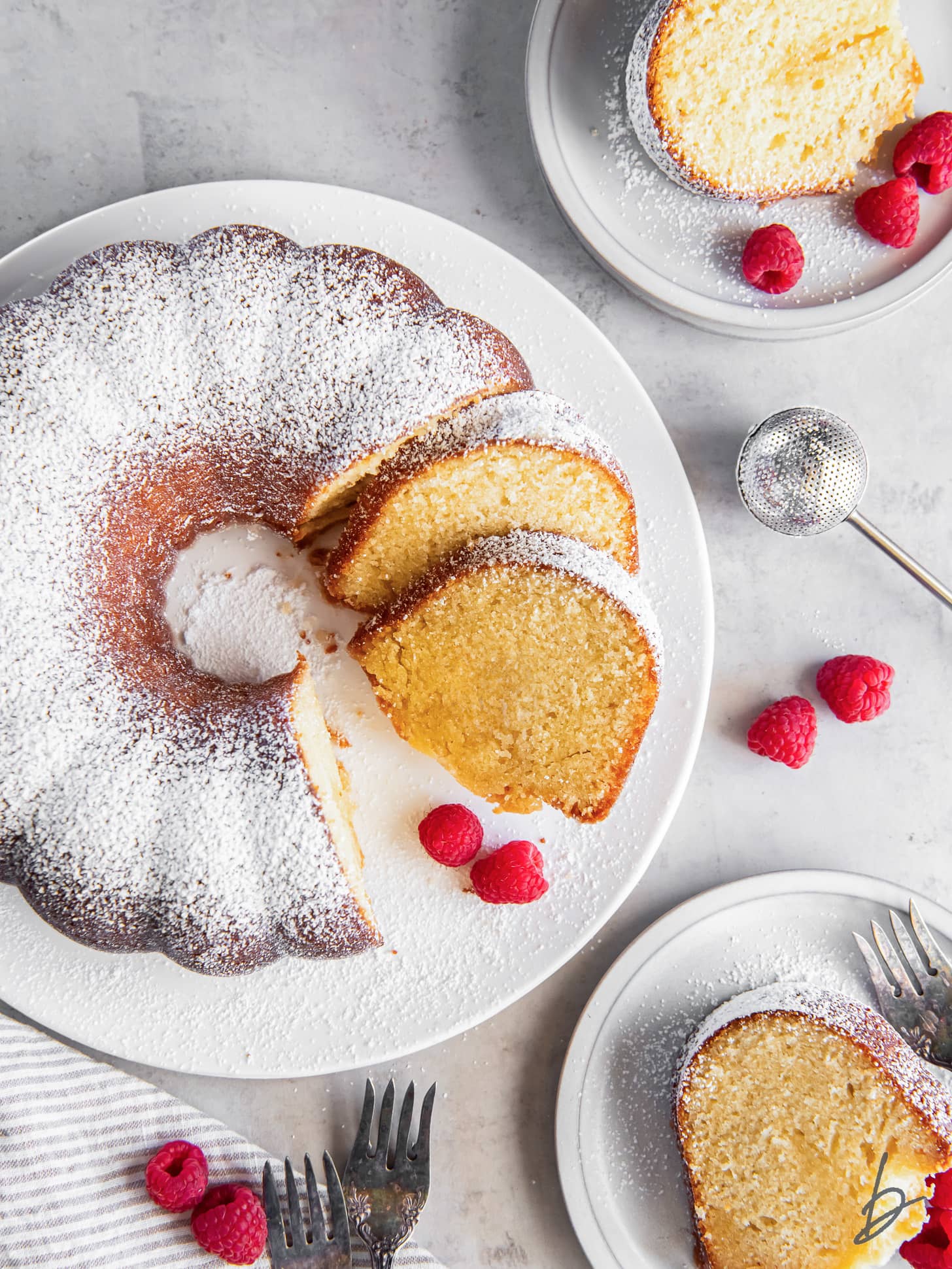 kentucky butter cake dusted with confectioners' sugar with a few slices cut and garnished with raspberries.