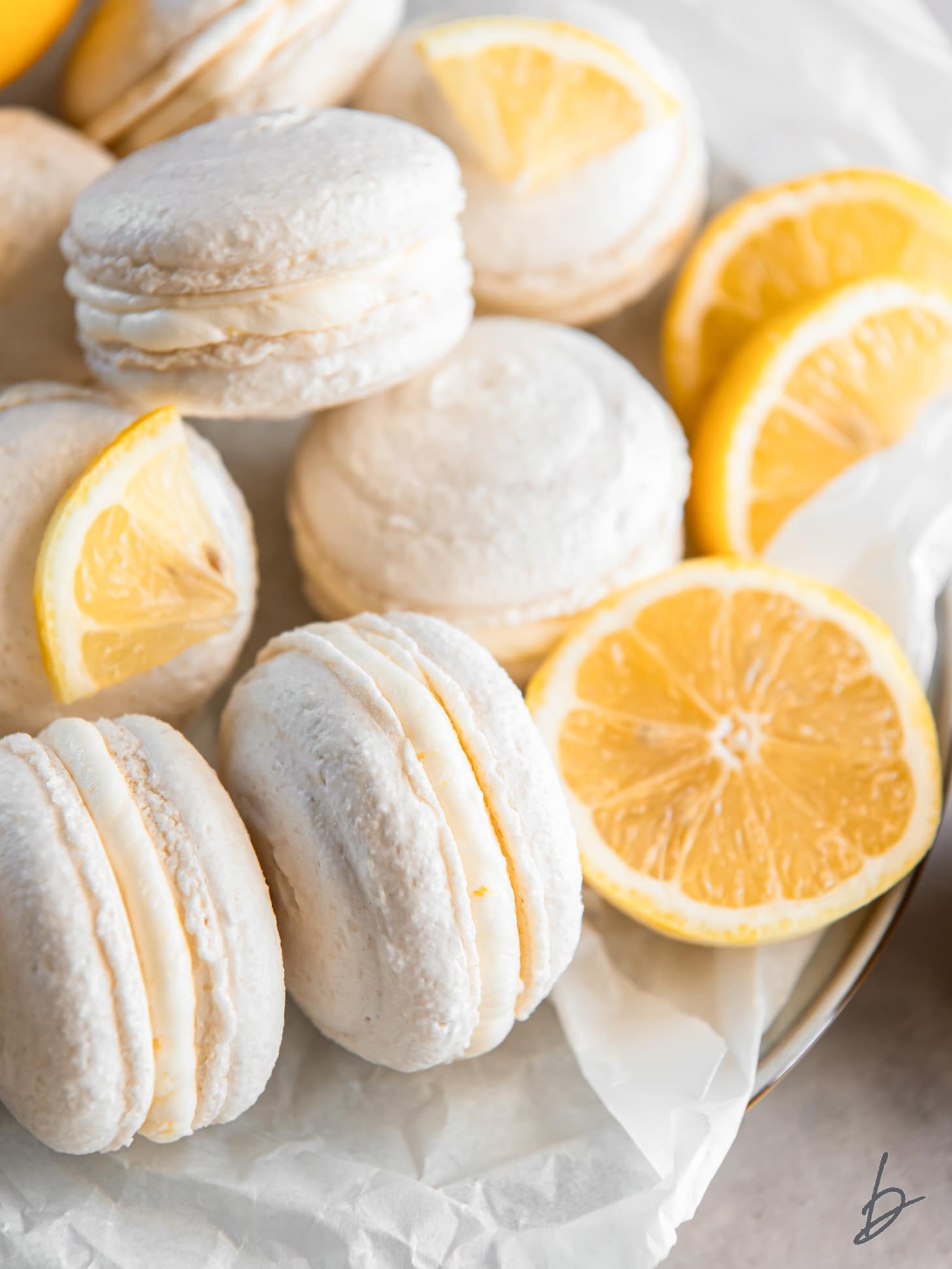 plate with macarons and lemon slices with one lemon macaron on its side showing lemon buttercream filling.