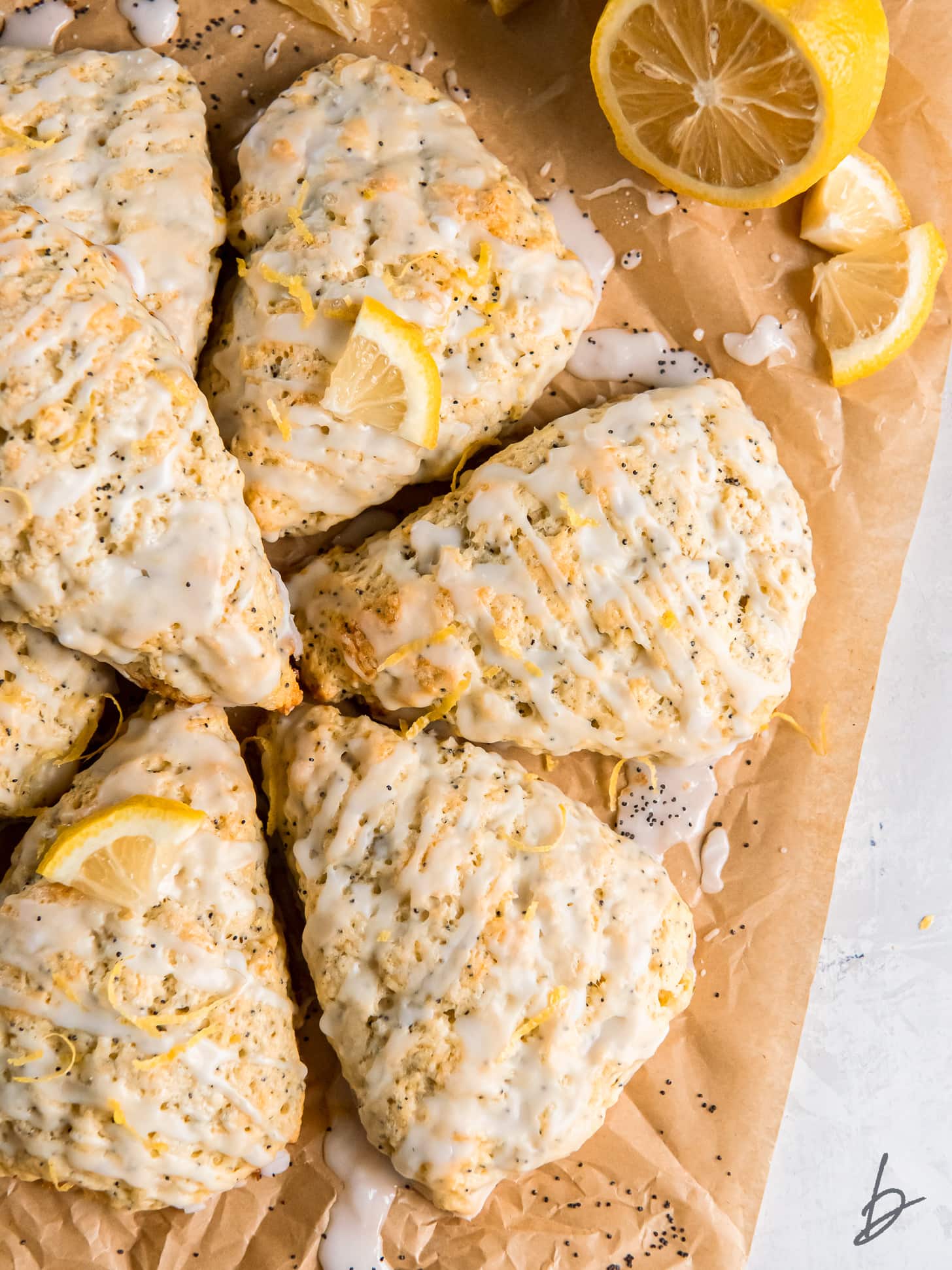 lemon poppy seed scones with glaze on parchment paper next to half a lemon.