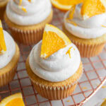 mimosa cupcake with an orange slice as garnish on wire cooling rack.