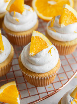 mimosa cupcake with an orange slice as garnish on wire cooling rack.
