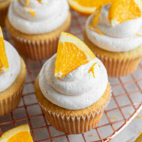 mimosa cupcake with an orange slice as garnish on wire cooling rack.