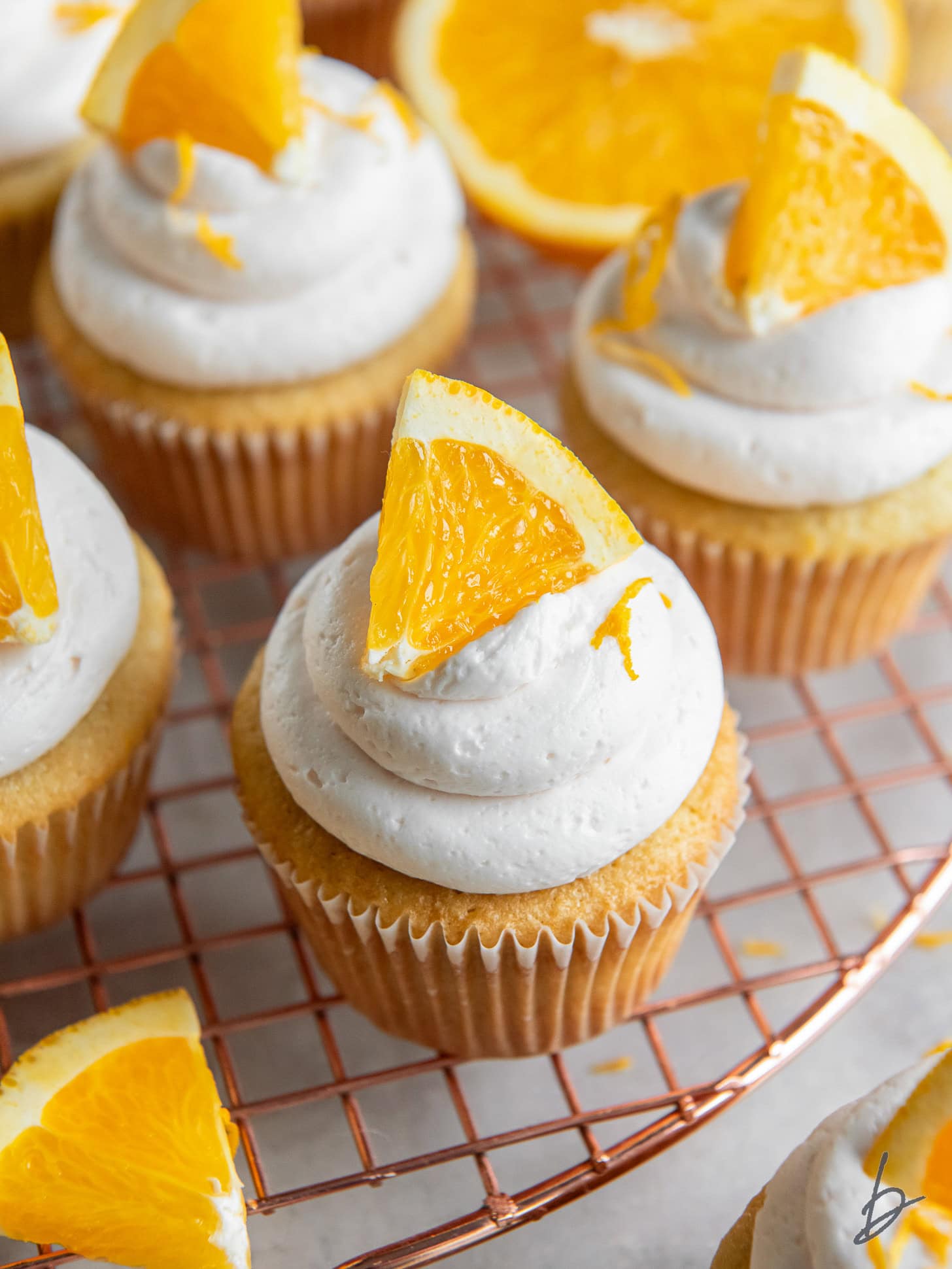 mimosa cupcake with an orange slice as garnish on wire cooling rack.