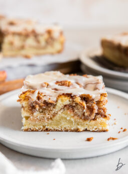 slice of honey bun cake on a plate showing layers of cinnamon brown sugar inside.