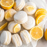 lemon macarons in a pile on parchment paper with lemon wedges.