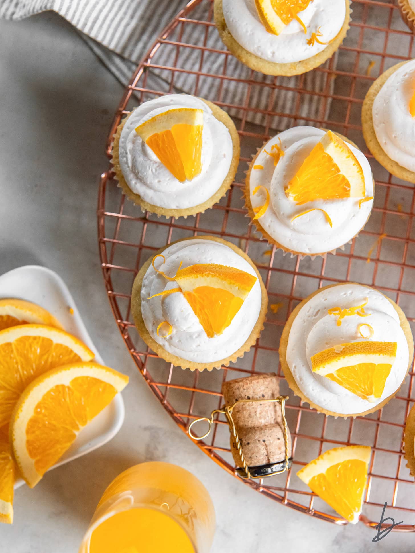 wire rack with mimosa cupcakes with champagne frosting and orange slice garnish.