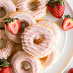 baked strawberry donuts with pink strawberry icing on a white round plate.