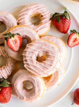 baked strawberry donuts with pink strawberry icing on a white round plate.