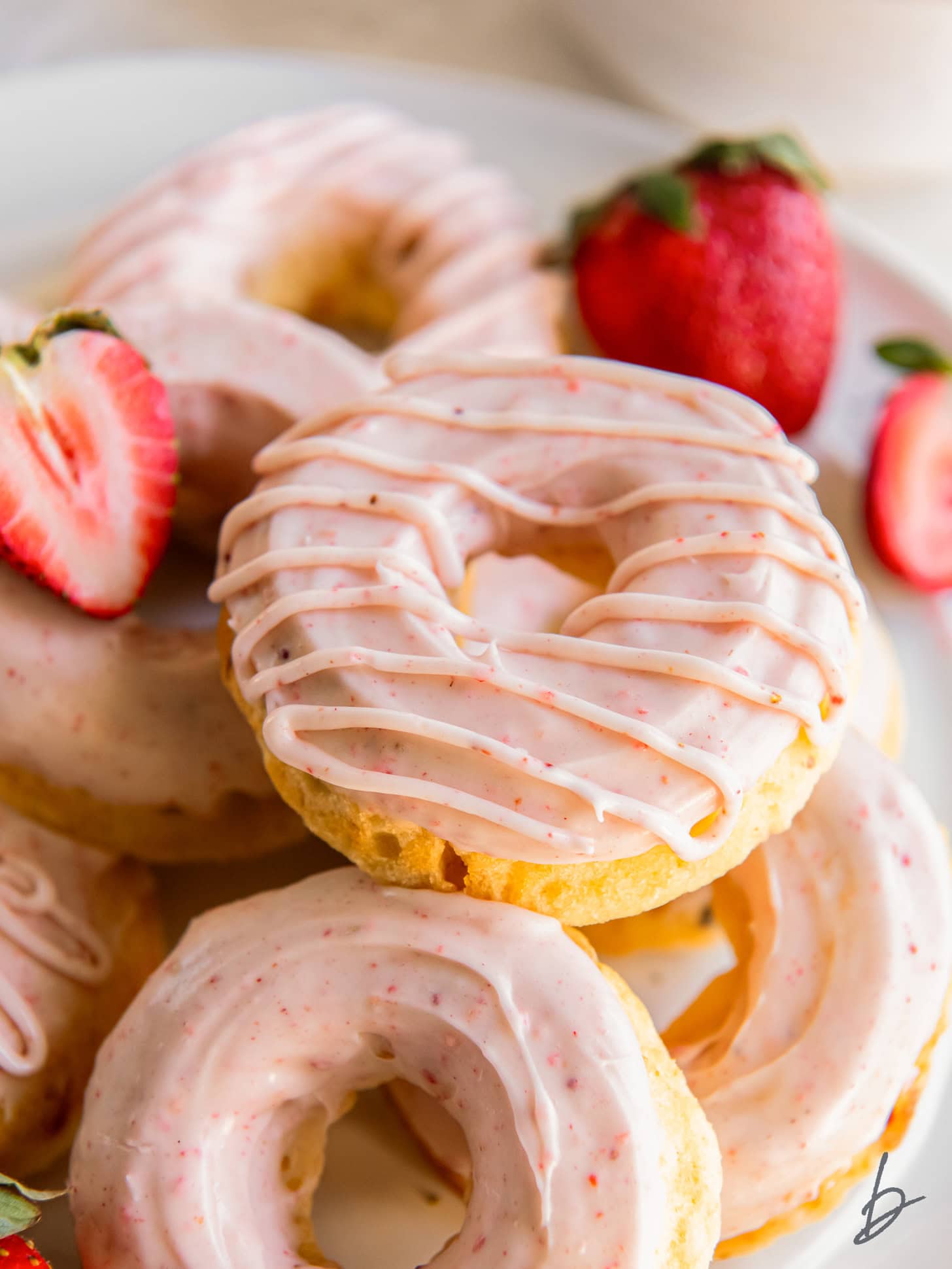 pink glazed strawberry donut on top of more donuts on a plate.