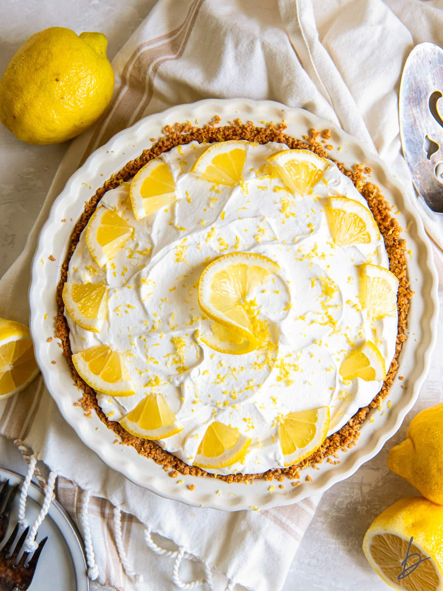 tabletop with uncut lemon icebox pie topped with whipped cream and lemon garnished.