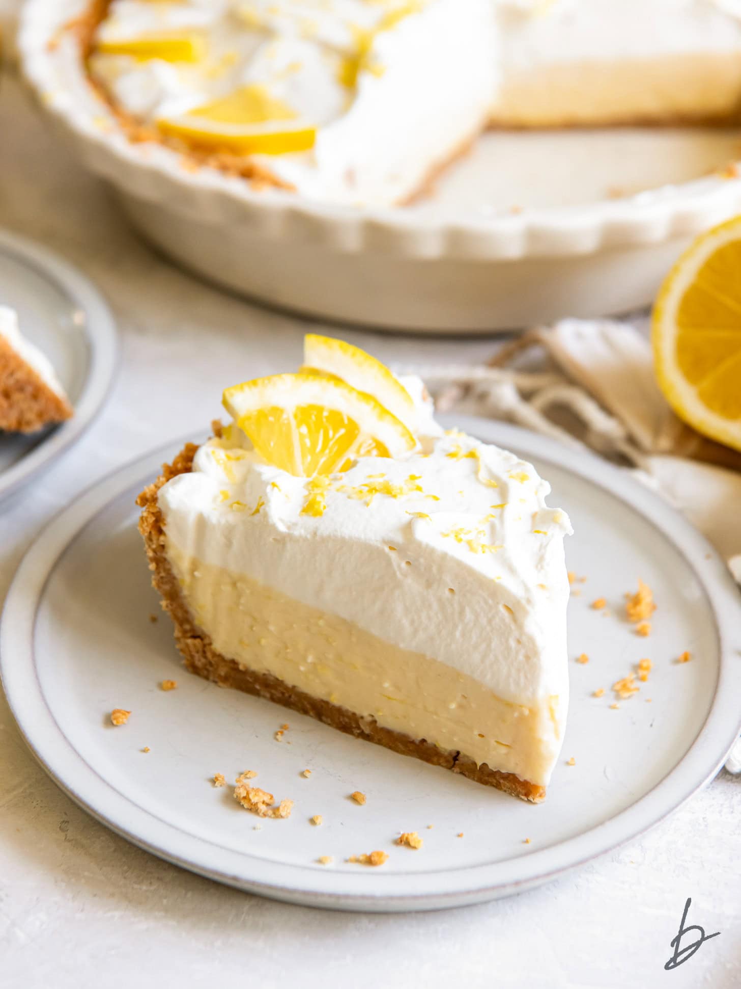 slice of lemon icebox pie with whipped cream and lemon slice garnish on a plate.