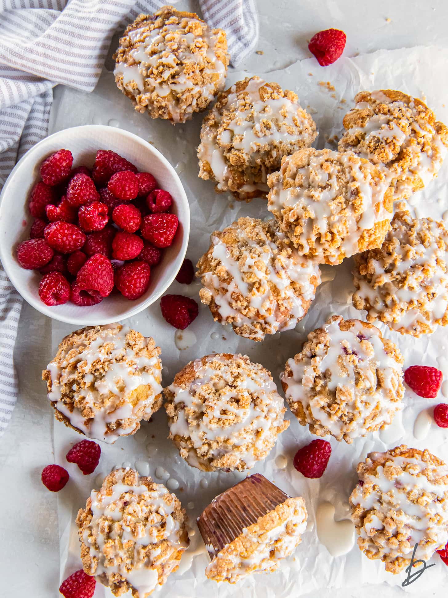 tabletop with raspberry muffins with streusel topping and lemon glaze.