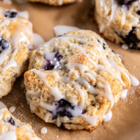 fresh lemon blueberry scone with glaze on parchment paper with a couple more scones.