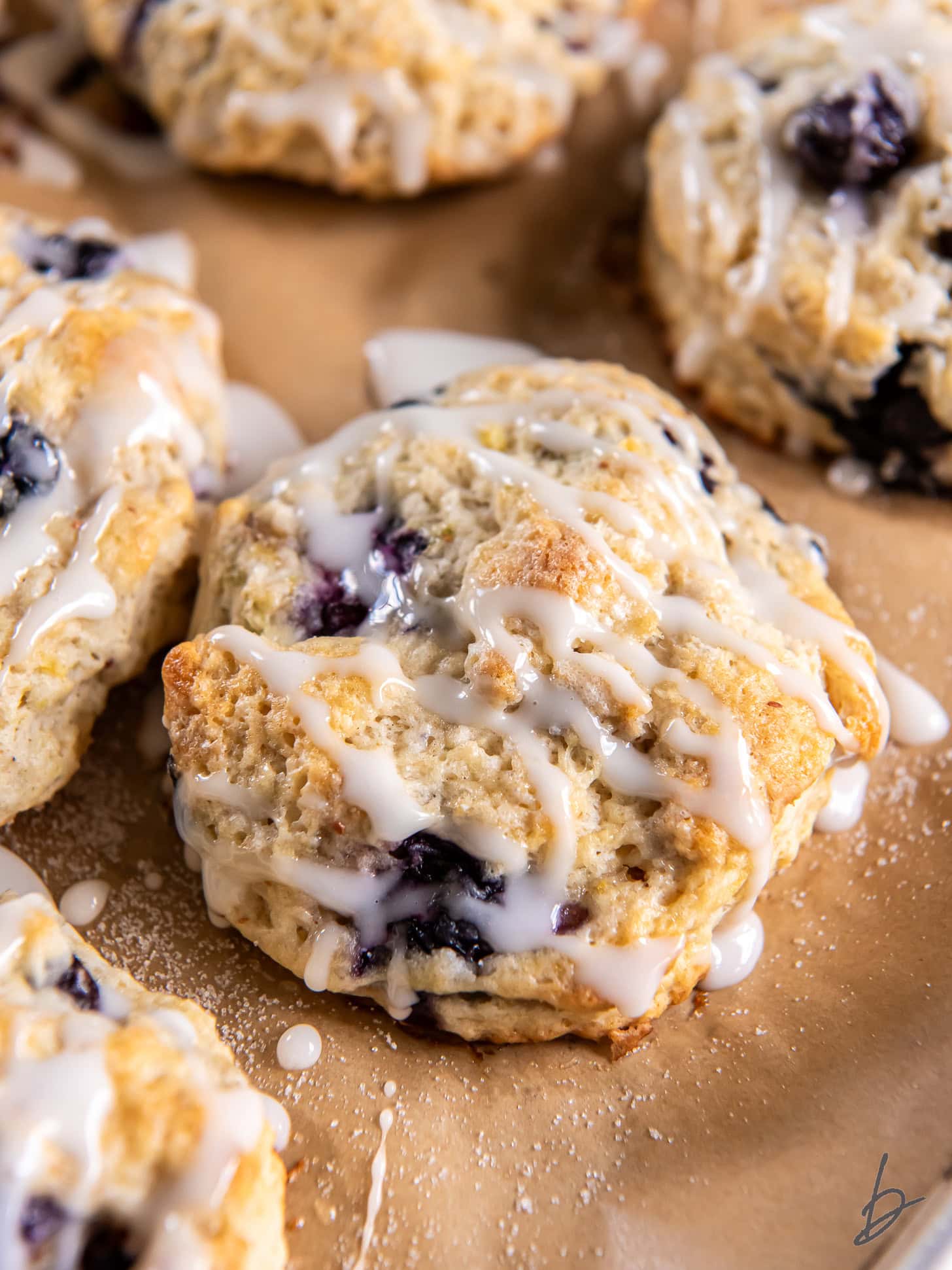 fresh lemon blueberry scone with glaze on parchment paper with a couple more scones.