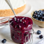 homemade blueberry sauce in a small glass jar with a spoon.