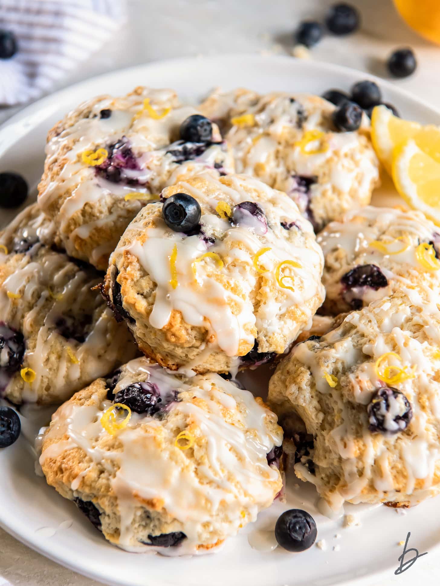 lemon blueberry scones with lemon glaze on a plate with a few fresh blueberries.