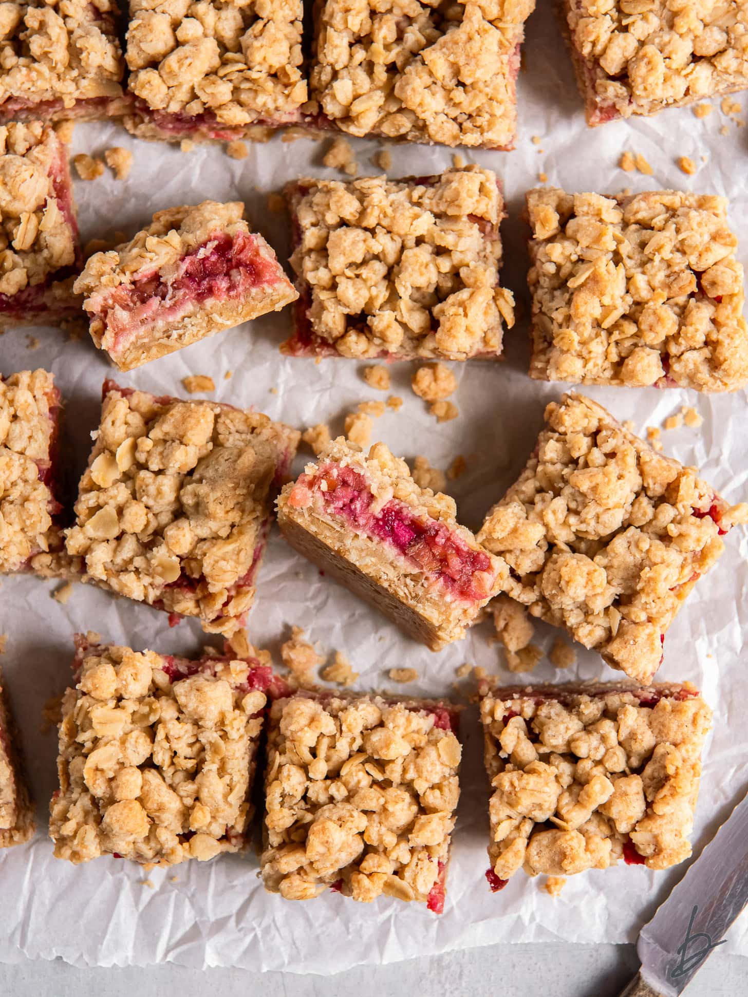 a couple rhubarb oatmeal bars on their side showing layers next to more bars on a tabletop.