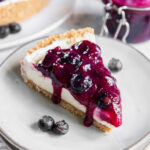 slice of no bake blueberry cheesecake on a plate with blueberry sauce.