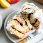 apple cinnamon roll cut in half on a plate with a knife.