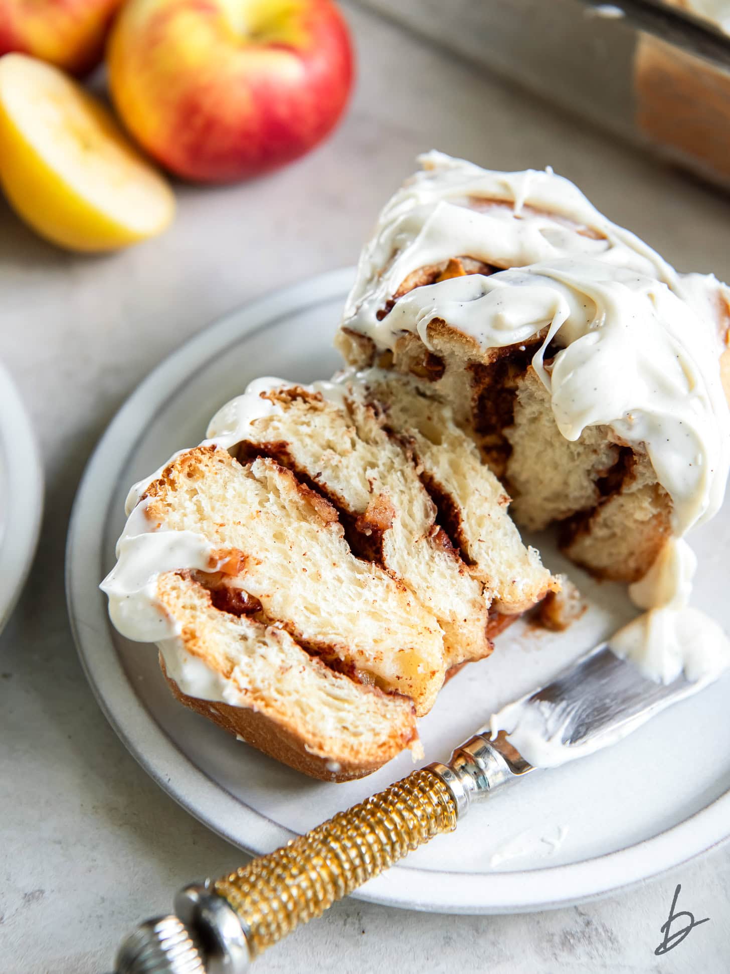 apple cinnamon roll cut in half on a plate with a knife.