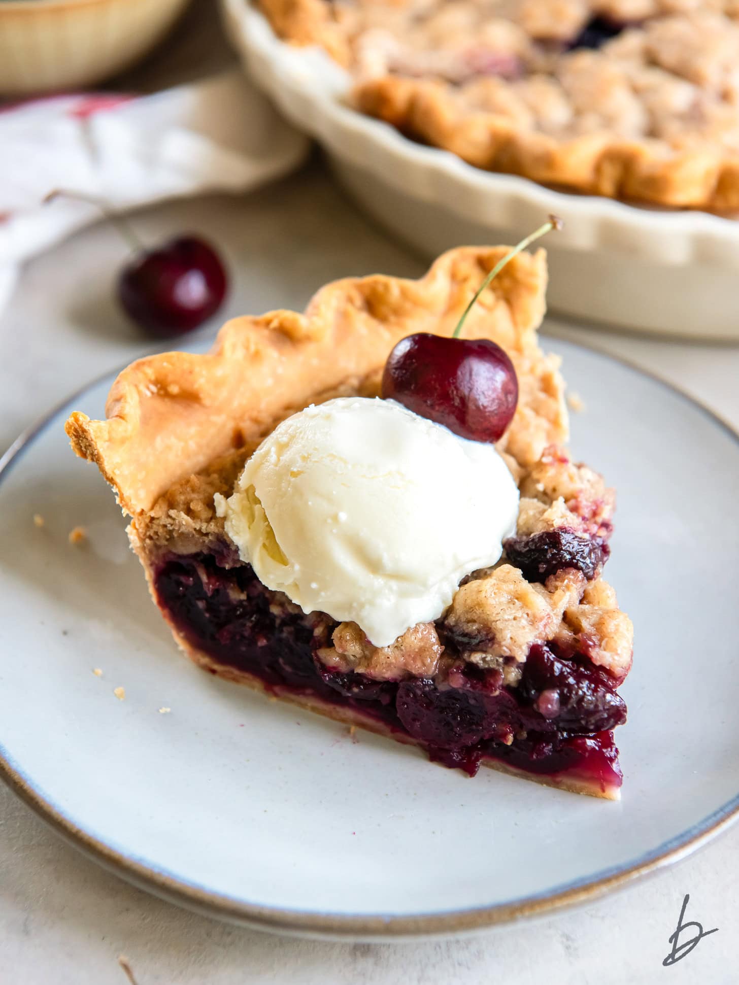 plate with slice of cherry crumble pie with scoop of vanilla ice cream on top.