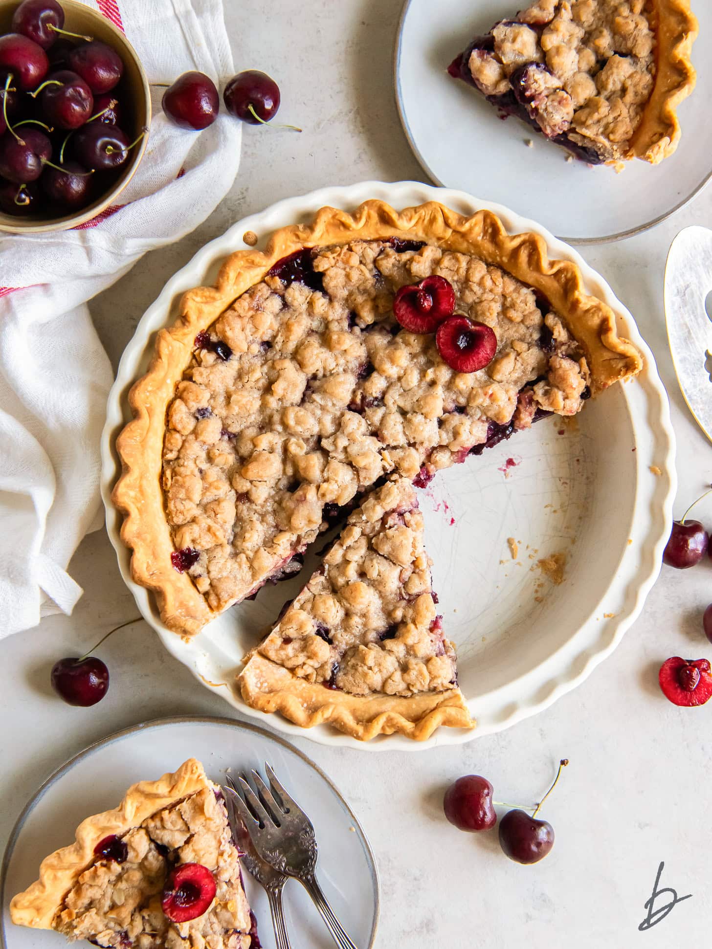 tabletop with cherry crumble pie with a few slices cut and put on plates.