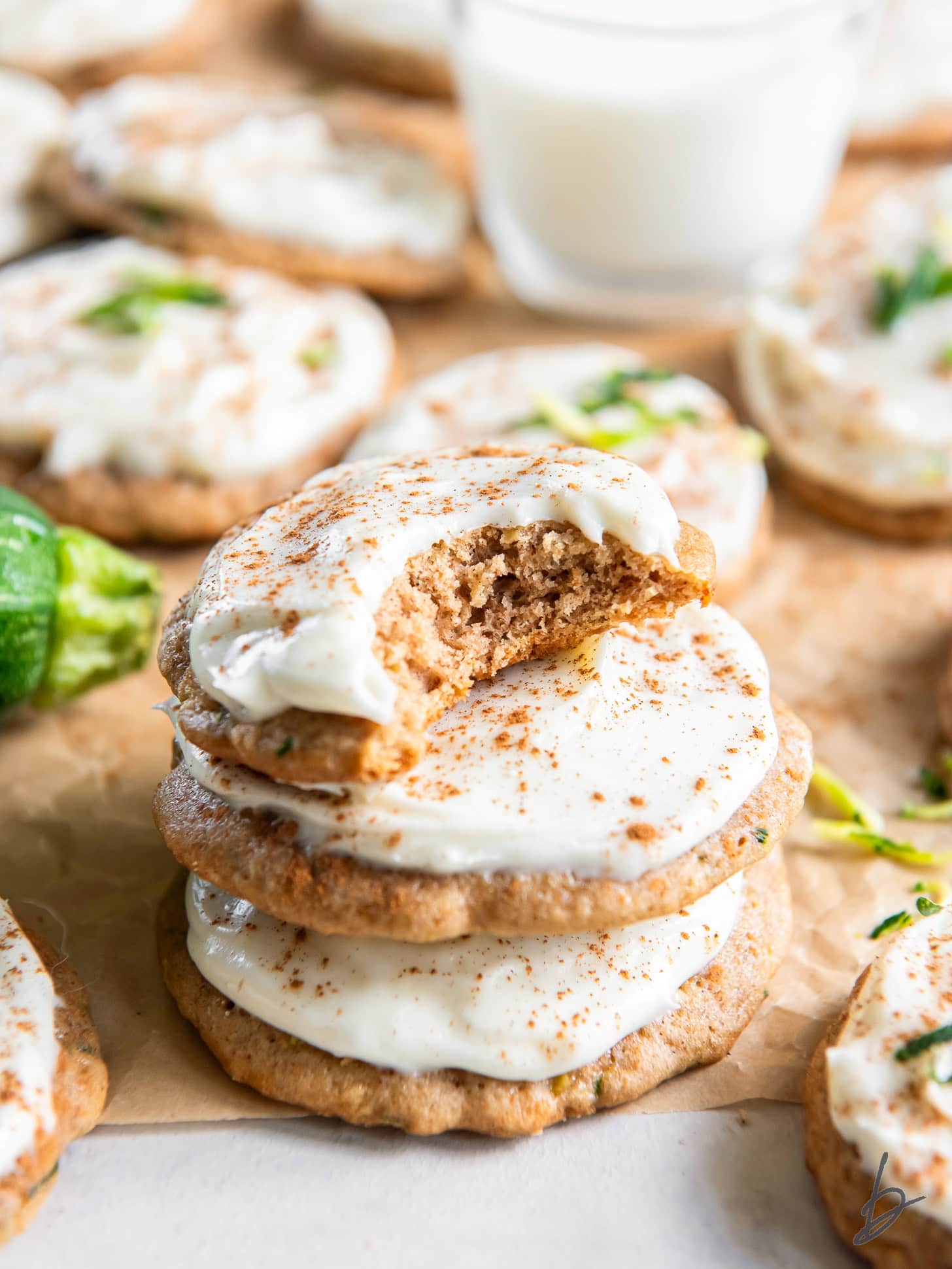 stack of frosted zucchini cookies with top cookie with a bite.