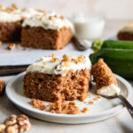 square slice of zucchini spice cake on a plate with a bite taken out of it by a fork.