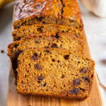 pumpkin banana bread sliced with chocolate chips leaning against loaf on cutting board.